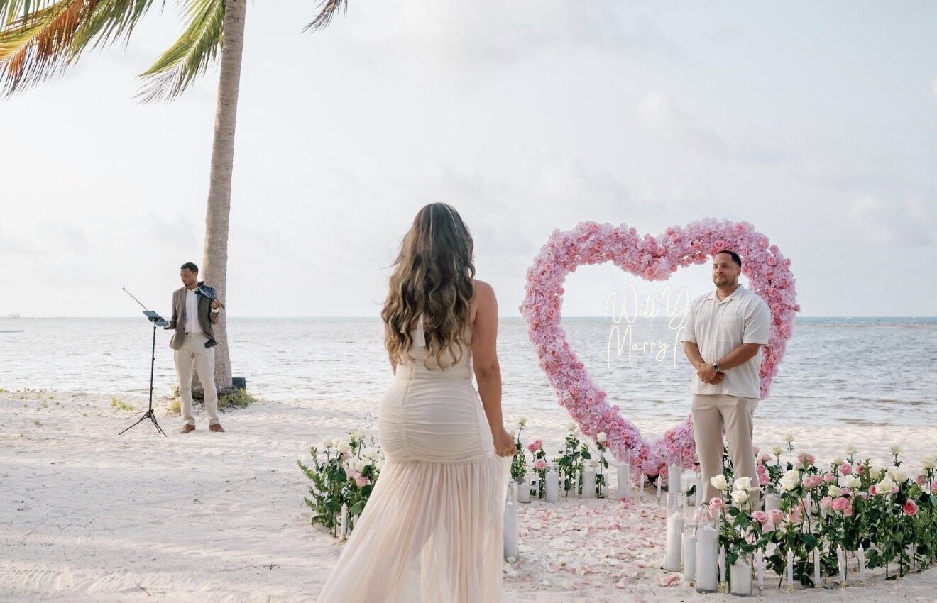 Bride walking toward a pink heart proposal arch with live violinist performing on the beach in Punta Cana