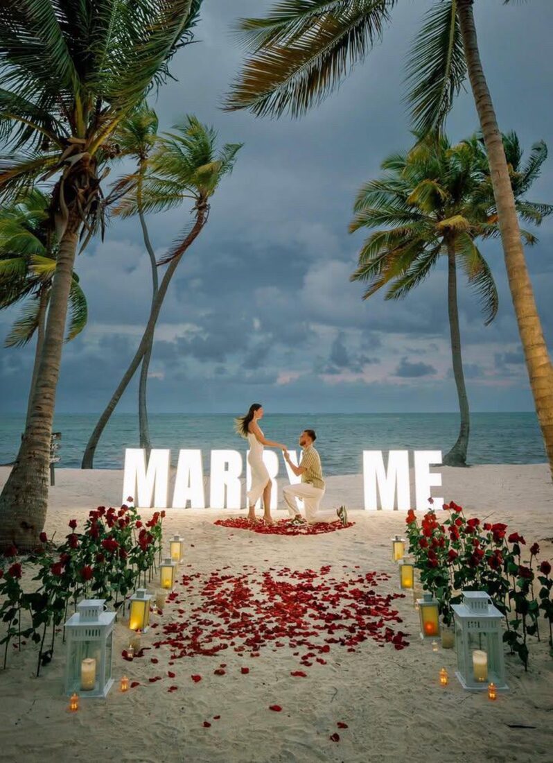 Beach marriage proposal in Punta Cana beneath glowing MARRY ME letters at dusk
