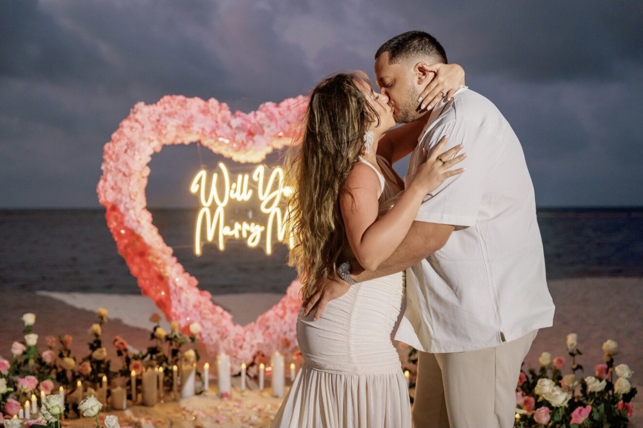Couple kissing in front of a pink rose heart proposal arch on the beach in Punta Cana